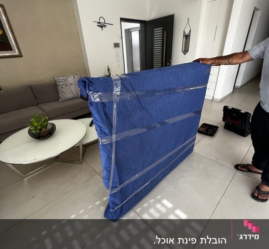 אדם מחזיק חפץ עטוף בכיסוי כחול עם סרט דבק